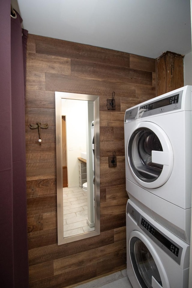 washroom featuring wood walls, stacked washer and clothes dryer, and hardwood / wood-style floors