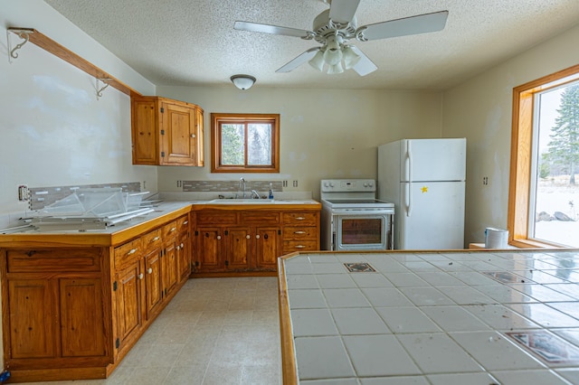 kitchen featuring white appliances, tile countertops, brown cabinets, a textured ceiling, and a sink