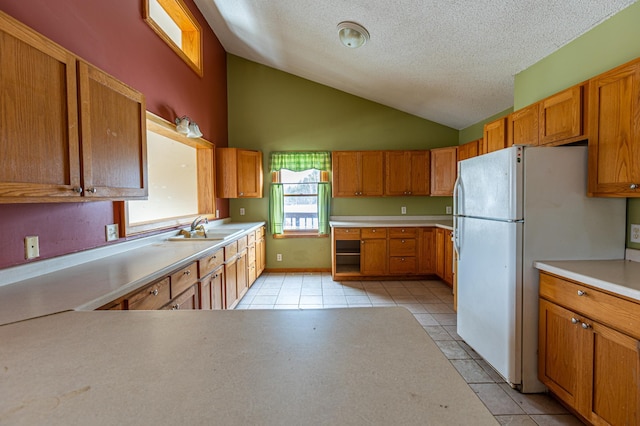 kitchen with freestanding refrigerator, vaulted ceiling, a sink, and light tile patterned flooring