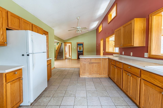 kitchen with lofted ceiling, freestanding refrigerator, a peninsula, light countertops, and light tile patterned flooring