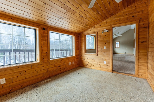 carpeted empty room featuring lofted ceiling, plenty of natural light, and wooden walls