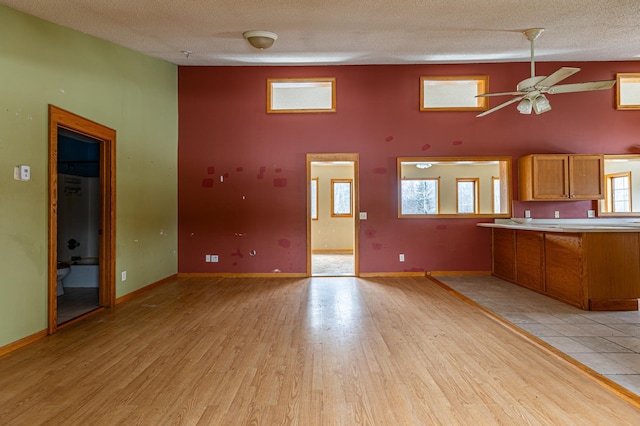 kitchen with a textured ceiling, baseboards, light countertops, light wood finished floors, and brown cabinetry