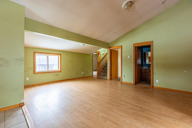 unfurnished room with light wood-type flooring, lofted ceiling, stairway, and a textured ceiling