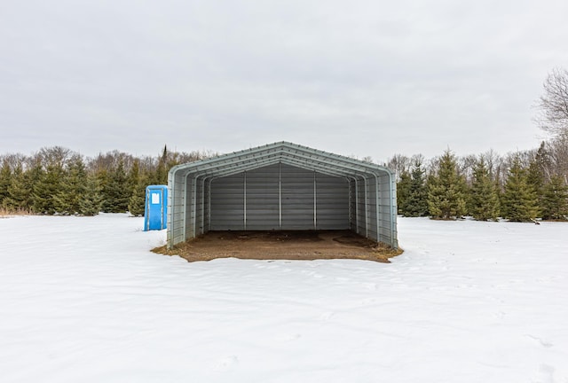 snow covered structure featuring a carport and a wooded view