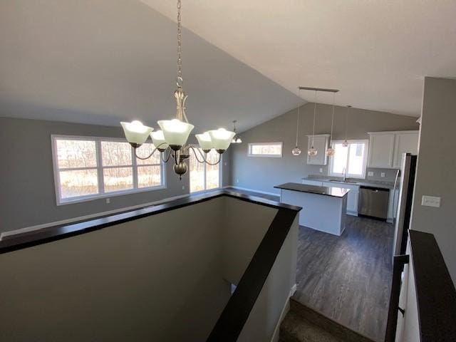 staircase featuring an inviting chandelier, dark wood-type flooring, sink, and vaulted ceiling