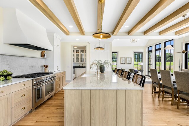 kitchen with premium range hood, an island with sink, sink, double oven range, and light wood-type flooring