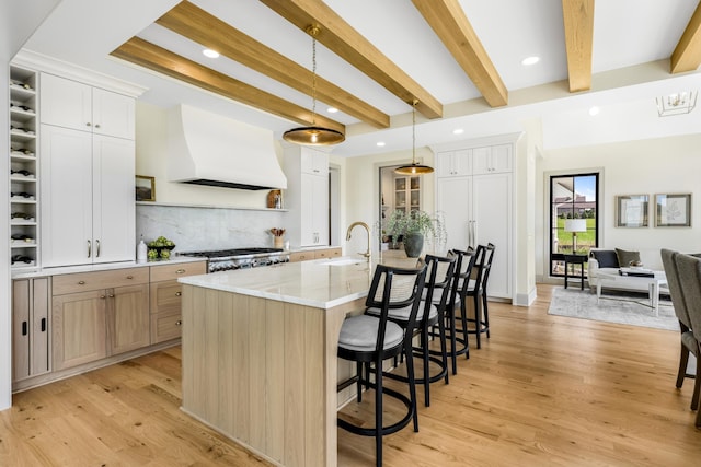 kitchen featuring white cabinets, hanging light fixtures, light wood-type flooring, and a large island with sink