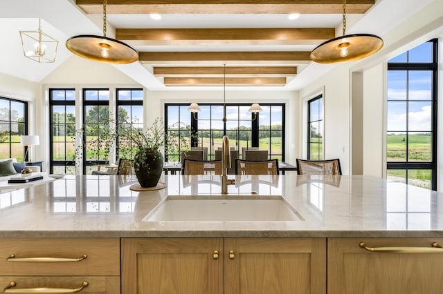 kitchen featuring sink, beamed ceiling, light stone counters, and decorative light fixtures