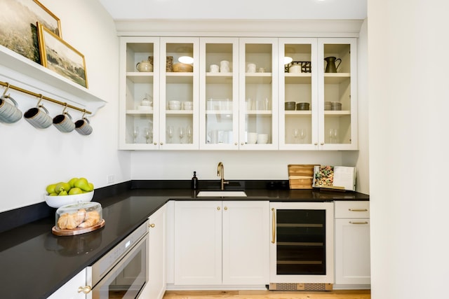 bar featuring beverage cooler, light hardwood / wood-style flooring, sink, and white cabinetry