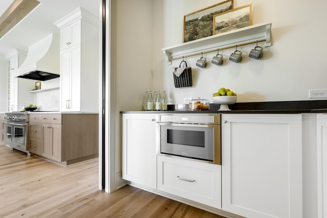 kitchen with stainless steel appliances, white cabinets, light hardwood / wood-style floors, and premium range hood