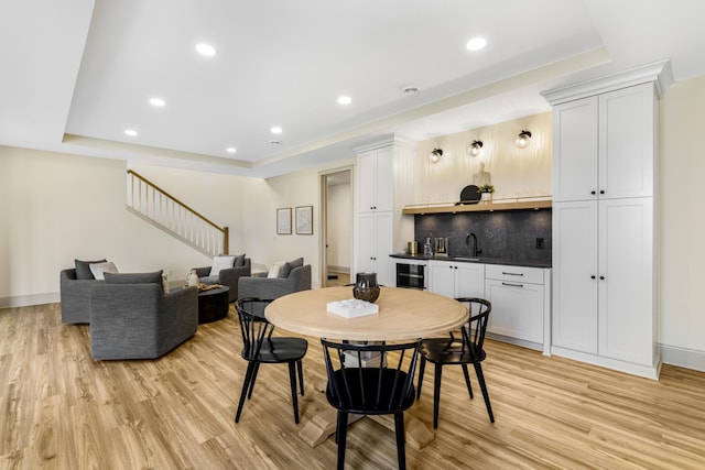 dining room featuring wine cooler, a tray ceiling, light wood-type flooring, and sink