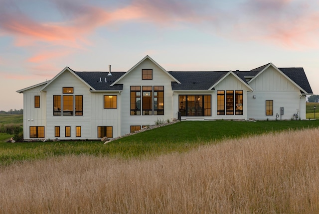 back house at dusk with a sunroom and a yard