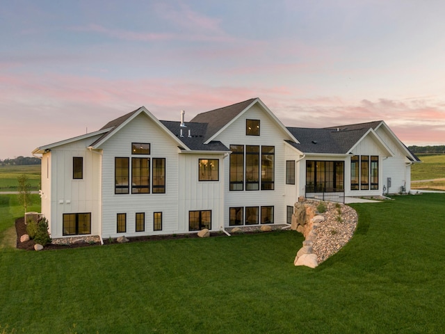 back house at dusk featuring a lawn and a sunroom