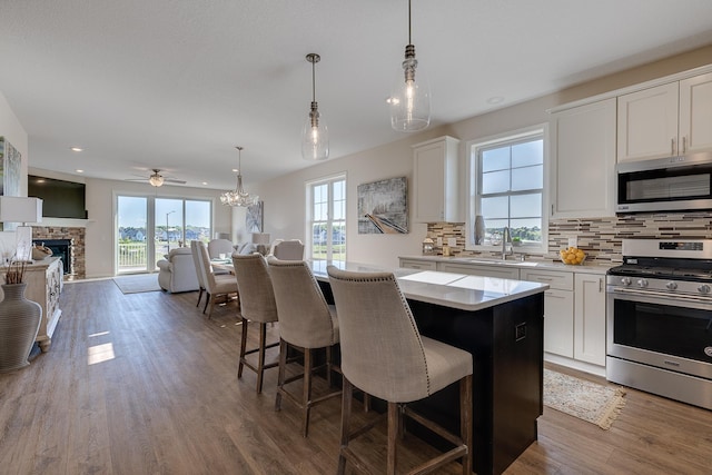 kitchen with pendant lighting, wood-type flooring, stainless steel appliances, a kitchen breakfast bar, and white cabinetry