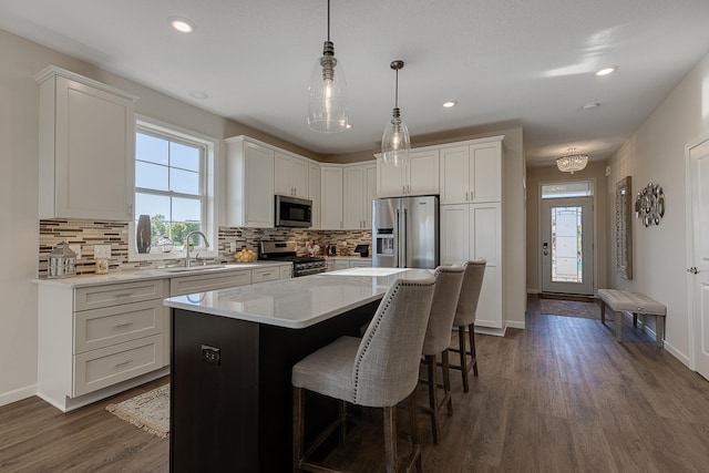 kitchen featuring appliances with stainless steel finishes, a center island, dark wood-type flooring, decorative light fixtures, and white cabinets