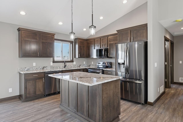 kitchen featuring pendant lighting, dark brown cabinets, stainless steel appliances, a center island, and light stone countertops