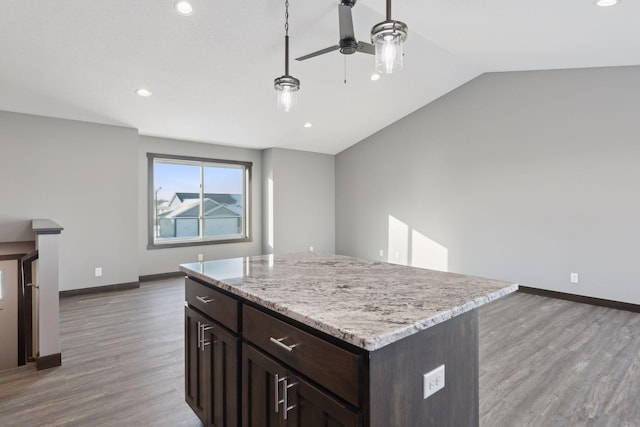 kitchen featuring vaulted ceiling, a kitchen island, decorative light fixtures, ceiling fan, and light hardwood / wood-style flooring