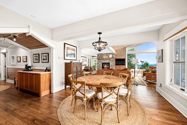 dining room with dark wood-type flooring, a fireplace, a notable chandelier, and vaulted ceiling