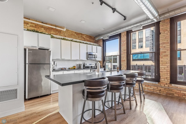 kitchen featuring appliances with stainless steel finishes, light hardwood / wood-style floors, white cabinetry, and brick wall