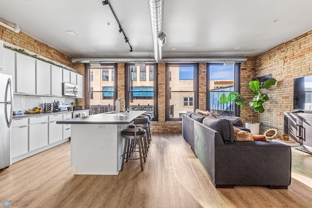 kitchen with white cabinets, stainless steel appliances, brick wall, and light hardwood / wood-style flooring