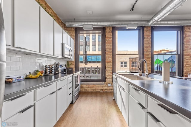 kitchen with white cabinets, sink, light hardwood / wood-style flooring, appliances with stainless steel finishes, and brick wall