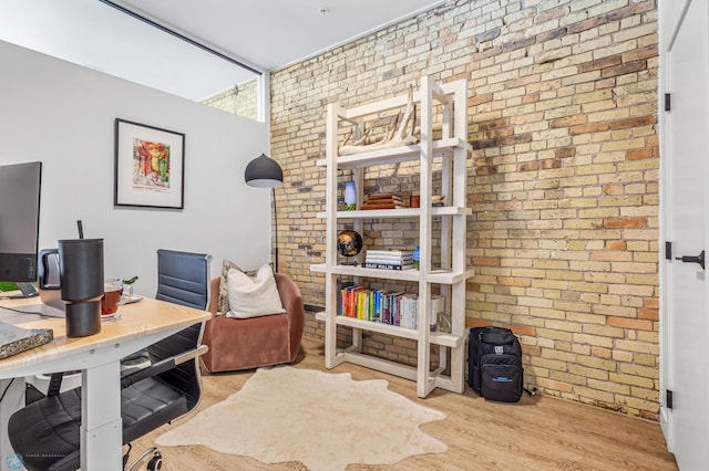 office area with light hardwood / wood-style floors and brick wall