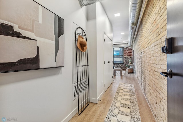 hall with light hardwood / wood-style flooring and brick wall