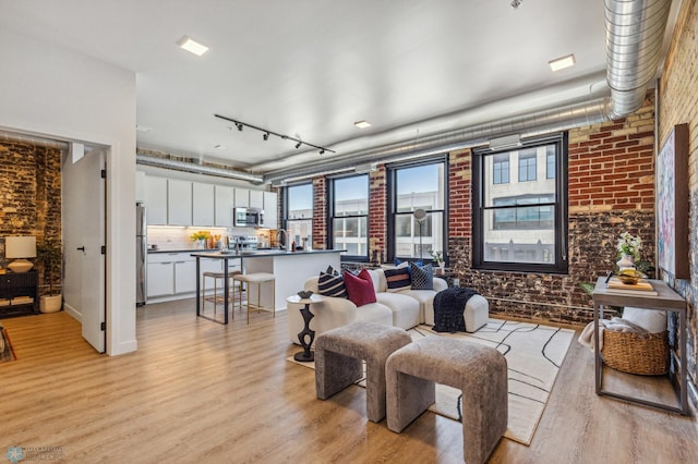 living room with rail lighting, brick wall, and light hardwood / wood-style floors