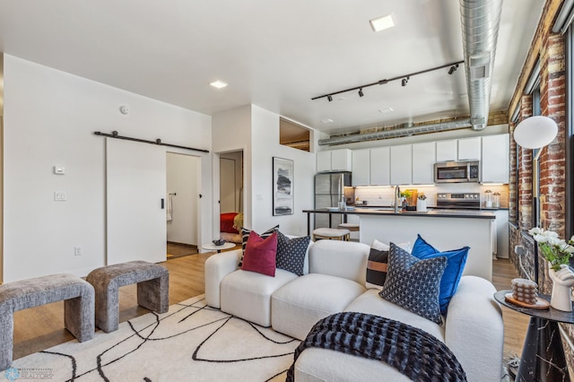 living room featuring track lighting, brick wall, sink, a barn door, and light hardwood / wood-style floors