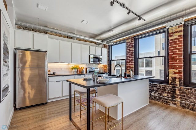 kitchen featuring white cabinets, brick wall, light hardwood / wood-style floors, and appliances with stainless steel finishes