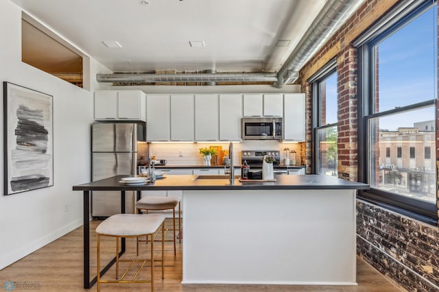 kitchen with a kitchen island with sink, white cabinetry, and stainless steel appliances