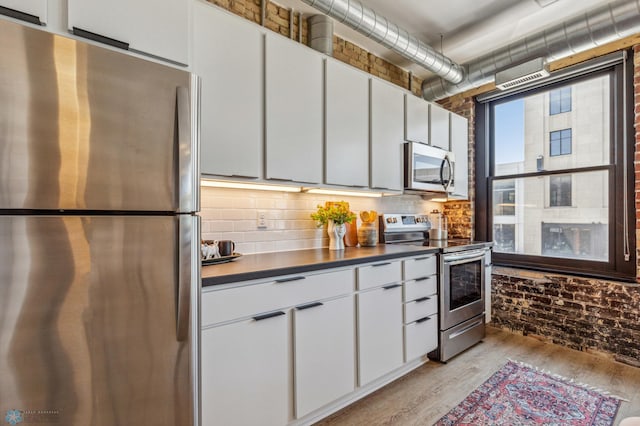 kitchen featuring white cabinetry, light hardwood / wood-style flooring, stainless steel appliances, and brick wall