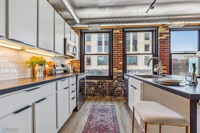 kitchen with white cabinetry, sink, stainless steel appliances, light hardwood / wood-style flooring, and brick wall