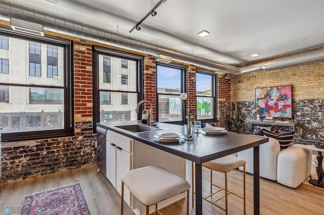 kitchen with white cabinetry, sink, brick wall, and light hardwood / wood-style flooring