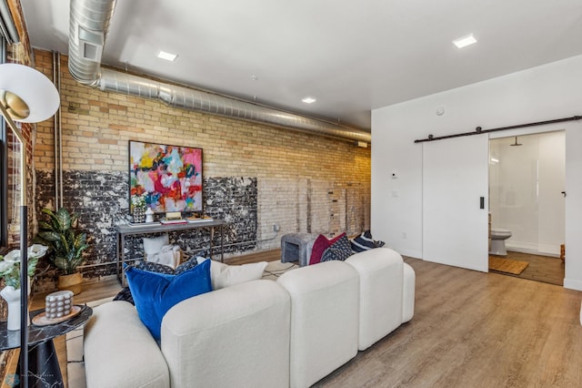 living room with a barn door, wood-type flooring, and brick wall