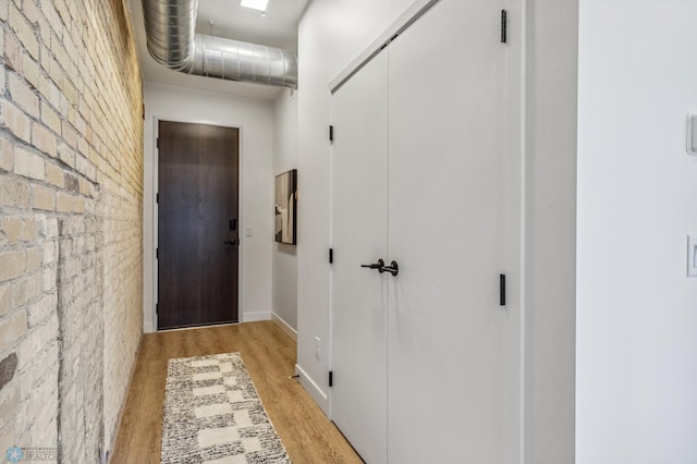 corridor with light hardwood / wood-style flooring and brick wall