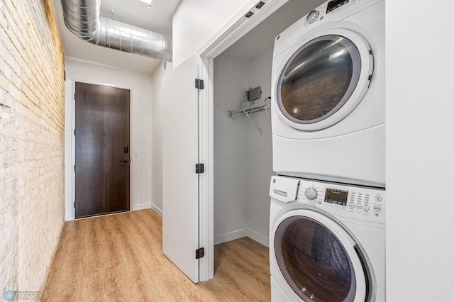 clothes washing area featuring stacked washing maching and dryer, brick wall, and light hardwood / wood-style flooring