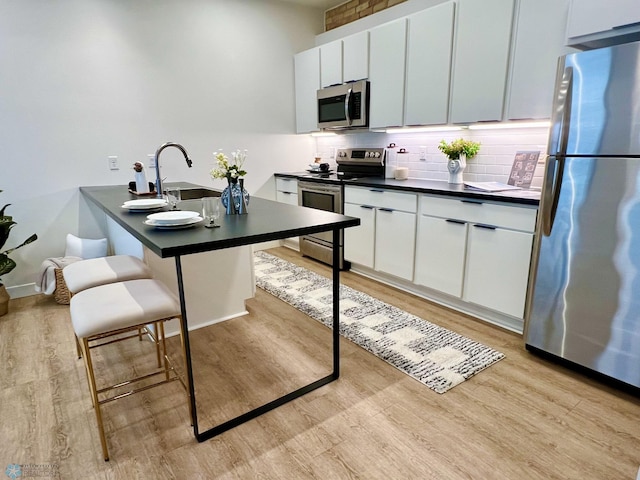 kitchen featuring sink, light hardwood / wood-style flooring, a kitchen bar, white cabinets, and appliances with stainless steel finishes