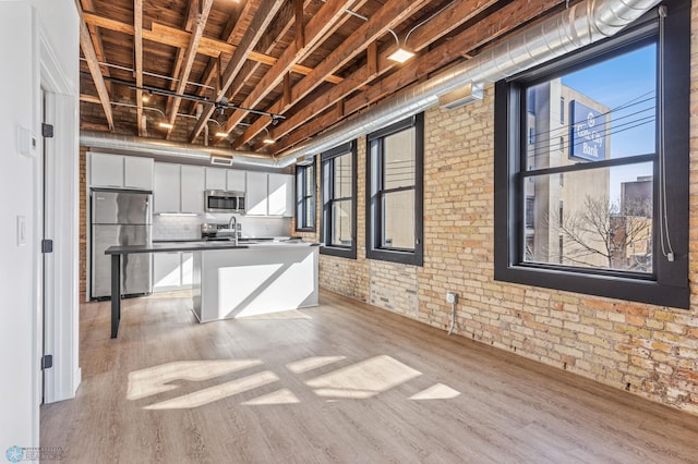 kitchen with a kitchen breakfast bar, light hardwood / wood-style flooring, appliances with stainless steel finishes, white cabinetry, and brick wall