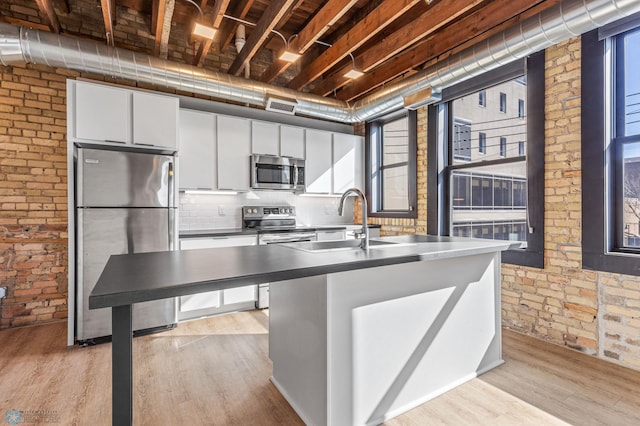 kitchen featuring sink, light hardwood / wood-style floors, white cabinetry, stainless steel appliances, and brick wall