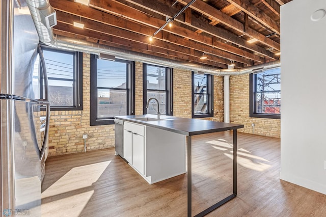 kitchen with brick wall, stainless steel appliances, sink, light hardwood / wood-style floors, and white cabinetry