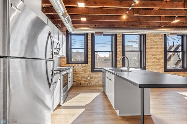 kitchen with white cabinetry, sink, brick wall, an island with sink, and appliances with stainless steel finishes