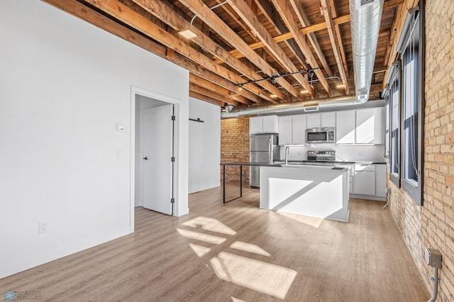 kitchen with white cabinetry, a center island, stainless steel appliances, brick wall, and light hardwood / wood-style floors