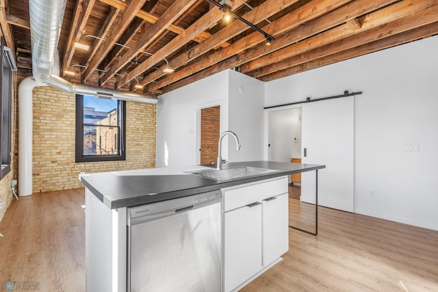 kitchen featuring dishwasher, white cabinets, sink, an island with sink, and brick wall