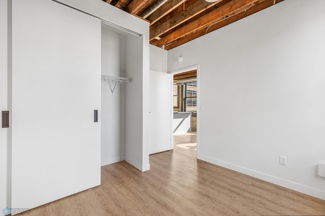 unfurnished bedroom featuring beam ceiling, light wood-type flooring, and a closet