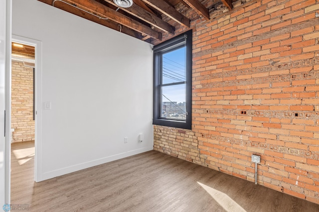 empty room featuring beam ceiling, light hardwood / wood-style flooring, and brick wall