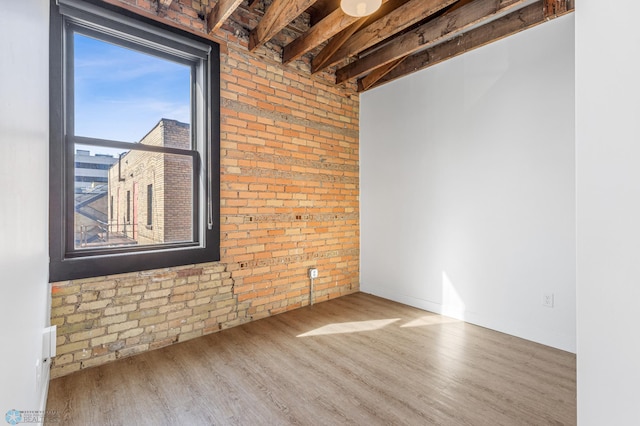 empty room with beamed ceiling, wood-type flooring, and brick wall