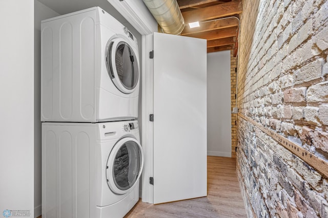 clothes washing area with light wood-type flooring, stacked washer / drying machine, and brick wall