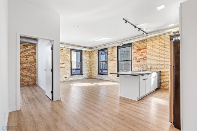 kitchen with stainless steel refrigerator, white cabinets, brick wall, and light wood-type flooring