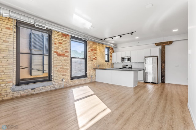 kitchen featuring kitchen peninsula, brick wall, stainless steel appliances, white cabinets, and light hardwood / wood-style floors